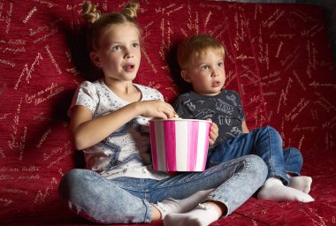 Çocuk sinema: bir kız ve bir erkek evde karanlıkta büyük bir kırmızı koltuk üzerinde bir film izlemek ve patlamış mısır yemek.