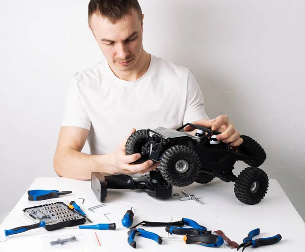 Hombre reparando un buggy de coche modelo controlado por radio. En la mesa hay herramientas para la reparación . — Foto de Stock