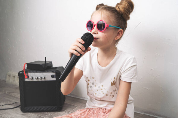 Домашнее выступление: молодая девушка сидит на полу и поет с микрофоном. Рядом стоит музыкальное оборудование
.