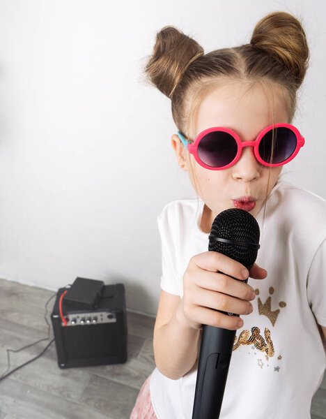 Молодая девушка поет с микрофоном у белой стены
.