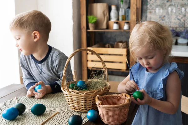 Święta Wielkanocne: dziecko dziewczynka i chłopiec malować jaja z pędzlem w kuchni. — Zdjęcie stockowe