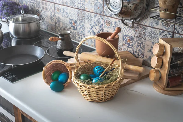 Húsvéti ünnepek: fonott kosárban színes festett tojás a konyhaasztalon. — Stock Fotó