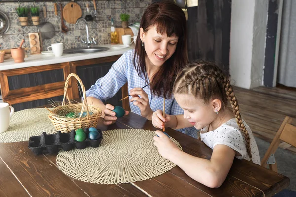 Easter holiday: mother and daughter paint eggs in the kitchen and put them in a basket.