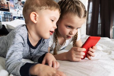 Çocuklar Gadget'ları: içine belgili tanımlık smartphone kıza şüpheci görünüyor çocuktur. Her iki yatağın üstüne yalan.