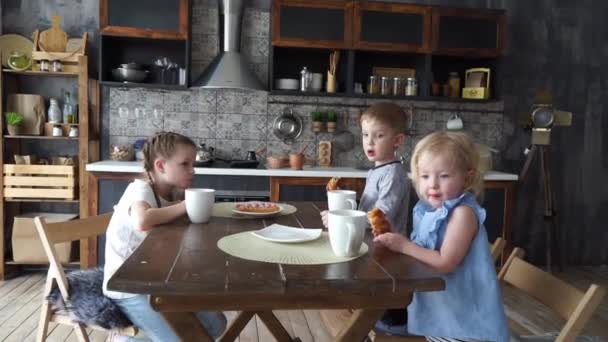 Family dinner: Three children at the kitchen table eating buns and drinking tea. — Stock Video