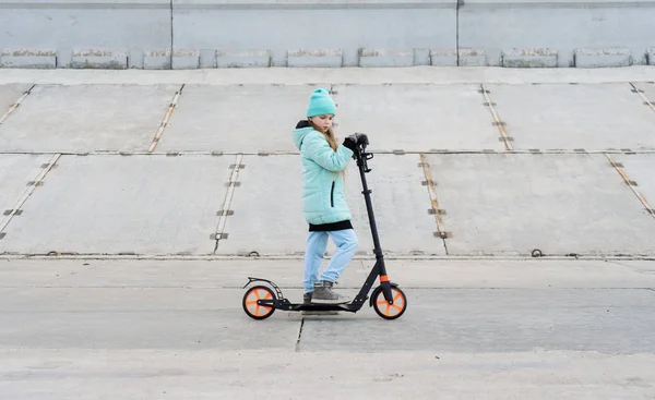 Harrastukset: Koulu tyttö sininen takki ratsastus skootteri harmaa betoni promenade . — kuvapankkivalokuva