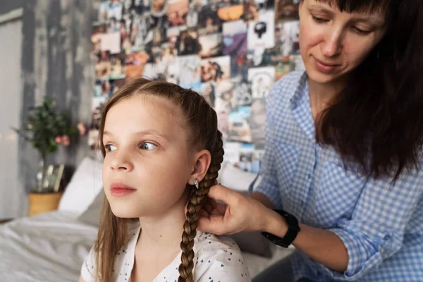Μαμά προσεκτικά πλεξούδες τα μαλλιά της αγαπημένης κόρες σε πλεξούδες στο κεφάλι της. — Φωτογραφία Αρχείου