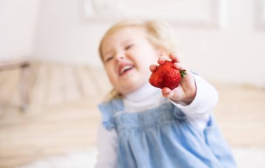 Çocuklar için meyve: mavi bir Sundress küçük iki yaşındaki kız elinde büyük bir çilek meyve tutar.