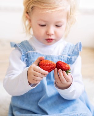 Çocuklar için meyve: mavi bir Sundress küçük iki yaşındaki kız elinde büyük bir çilek meyve tutar. Portre.