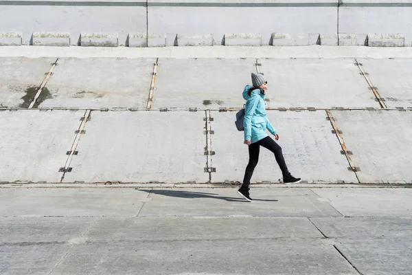Vue de profil : une fille vêtue d'une veste bleue saute sur une surface en béton . — Photo
