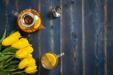 Mavi ahşap arka planda Deniz topalak çayı ve sarı lale ile şeffaf kupa ve çaydanlık.