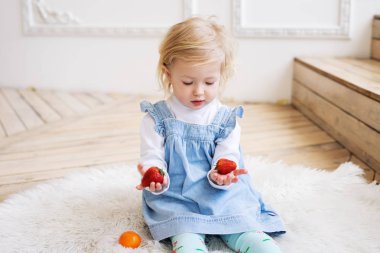 Çocuklar için meyve: mavi bir Sundress küçük iki yaşındaki kız elinde büyük bir çilek meyve tutar.