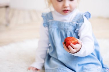 Çocuklar için meyve: mavi bir Sundress küçük iki yaşındaki kız elinde büyük bir çilek meyve tutar.