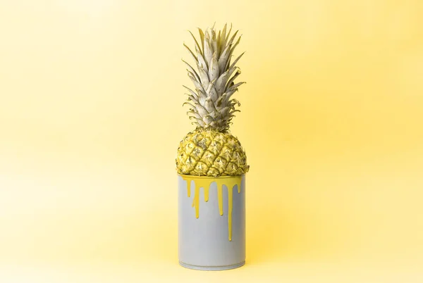 Creative idea: pineapple in a can with yellow paint on a uniform yellow background.