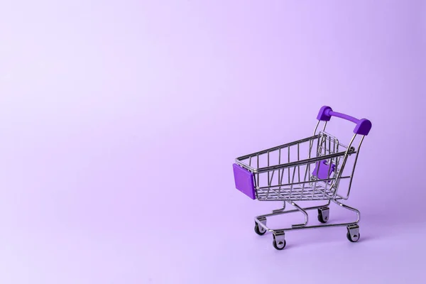 Compras das mulheres: um carrinho roxo em miniatura vazio de um supermercado em um fundo roxo . — Fotografia de Stock