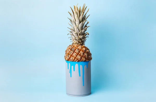 Creative idea: pineapple in a can with blue paint on a uniform blue background.