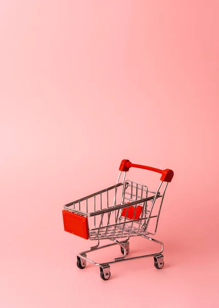 Womens shopping: an empty miniature trolley from a supermarket on a pink background. — Stock Photo, Image