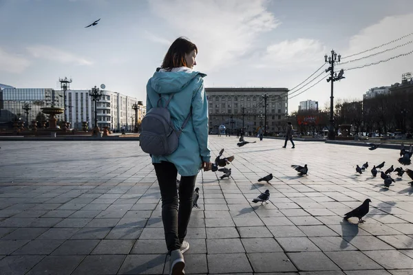 ストリート写真:女の子の観光客が鳩の間で町の広場を歩きます。背面のバックパック. — ストック写真