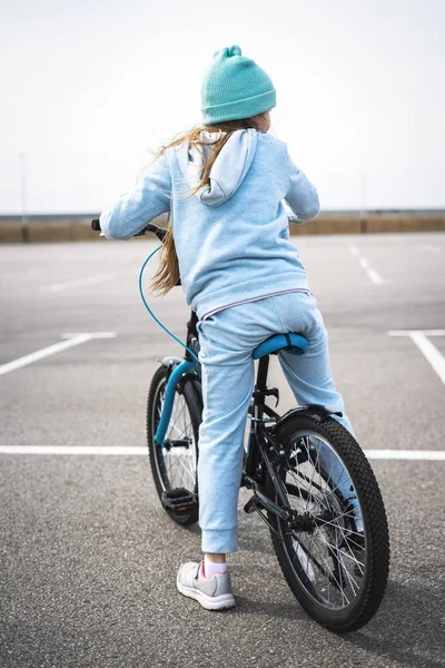 Een meisje in een hoed en een blauwe trui op een fiets gestopt en kijkt rond. — Stockfoto