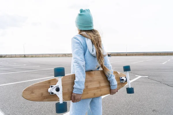 Een meisje in een hoed en een blauwe trui houdt een groot Longboard. — Stockfoto