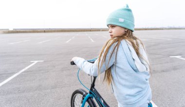 Şapkalı bir kız ve bisikletli mavi bir kazak durdu ve etrafa bakıyor..