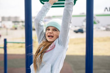 Mavi şapkalı kız yatay barda asılı..