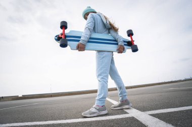 Şapkalı ve mavi kazaklı bir kız elinde büyük bir uzun tahta tutuyor..