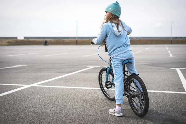 Een meisje in een hoed en een blauwe trui op een fiets gestopt en kijkt rond. — Stockfoto