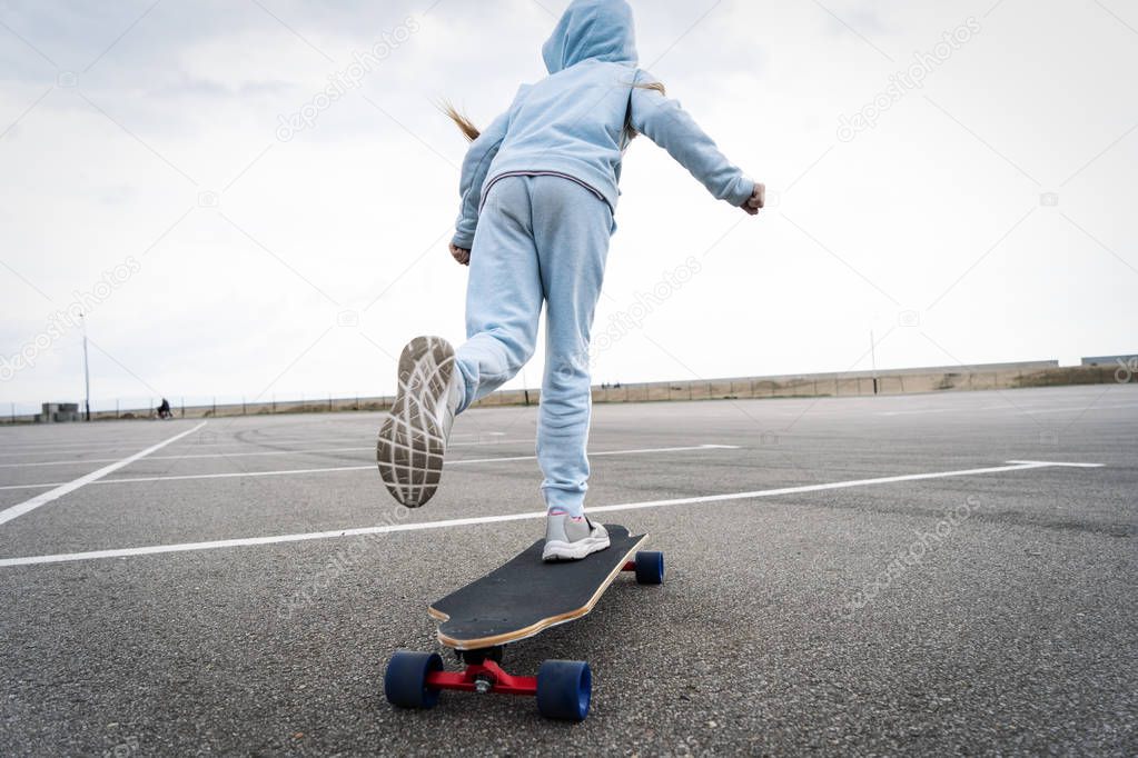 Street sports: A girl in a blue sweater pushes off with her foot and quickly rolls on a longboard.