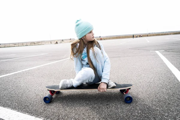 Уличные виды спорта: девушка в синем свитере и кепке быстро катается на лонгборде . — стоковое фото