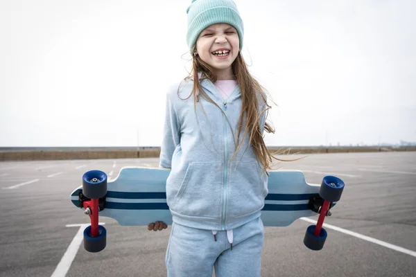 Een meisje in een hoed en een blauwe trui houdt een groot Longboard. — Stockfoto