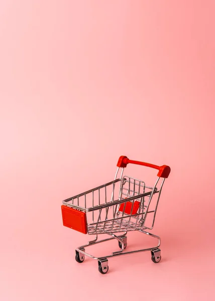 Red miniature trolley from a supermarket on a pink background. Close-up. — Stock Photo, Image