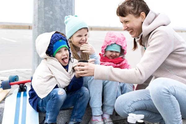 Moeder giet hete thee van een thermos voor drie kinderen. De kinderen skaten op een skateboard en bevroor. — Stockfoto