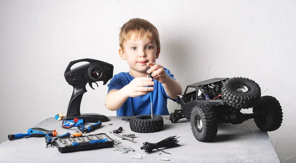 Modelagem de rádio obby: um menino em uma camiseta azul reparando um buggy de carro controlado por rádio com uma chave de fenda . — Fotografia de Stock
