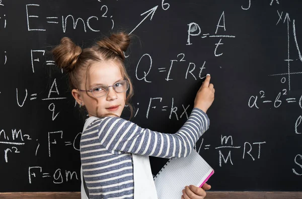 Zpátky do školy: chytrá dívčí školka píše na tabuli složité vzorce v křídě. Portrét. — Stock fotografie
