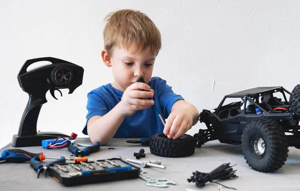 Modelagem de rádio obby: um menino em uma camiseta azul reparando um buggy de carro controlado por rádio com uma chave de fenda . — Fotografia de Stock