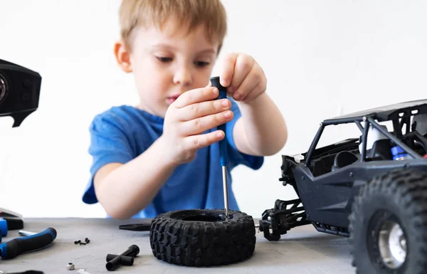 Modelagem de rádio obby: um menino em uma camiseta azul reparando um buggy de carro controlado por rádio com uma chave de fenda . — Fotografia de Stock