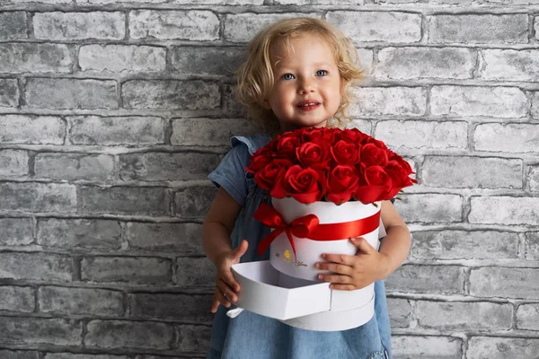 Una niña pequeña con un gran ramo de rosas en una caja blanca redonda enferma . — Foto de Stock