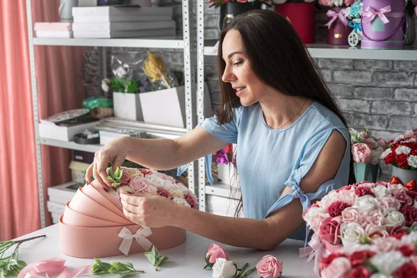 A florist girl is preparing a large bouquet in a pink box for a childs birthday party.