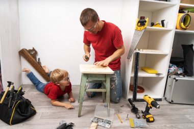 Baba küçük oğluna tornavidayla vidaları nasıl sıkacaklarını gösteriyor..