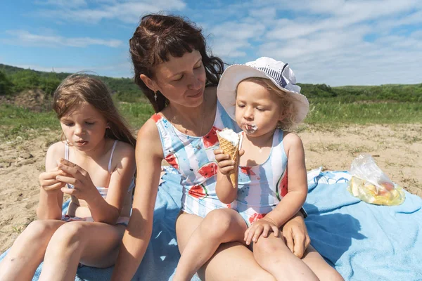 Mamá y los niños están sentados en la arena junto al mar . — Foto de Stock