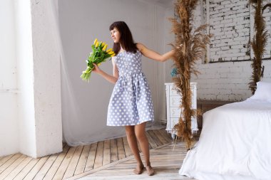 Mavi benekli elbiseli bir kız elinde tutar ve sarı lalebüyük bir buket koklar.