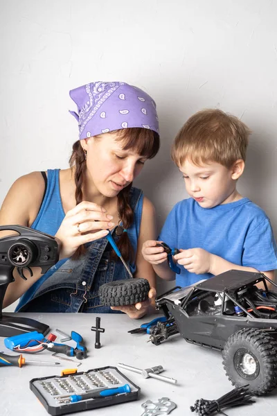 Mulheres no trabalho dos homens: Mãe ajuda seu filho com a fixação de um modelo de buggy controlado por rádio . — Fotografia de Stock