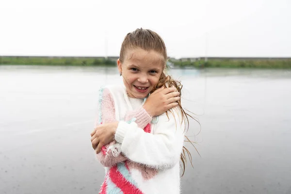 Een gelukkig schoolmeisje wordt nat in de regen en lacht. — Stockfoto