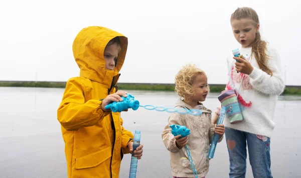 雨の日にレインコートを着た少年と少女が泡を吹く. — ストック写真