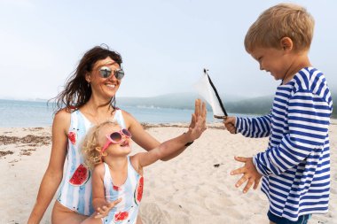 Anne ve aynı mayo ve güneş gözlüğü iki kızı kum üzerinde yatıyor ve dil göstermek. Pembe güneş gözlüğü kıvırcık saçlı küçük kızı.