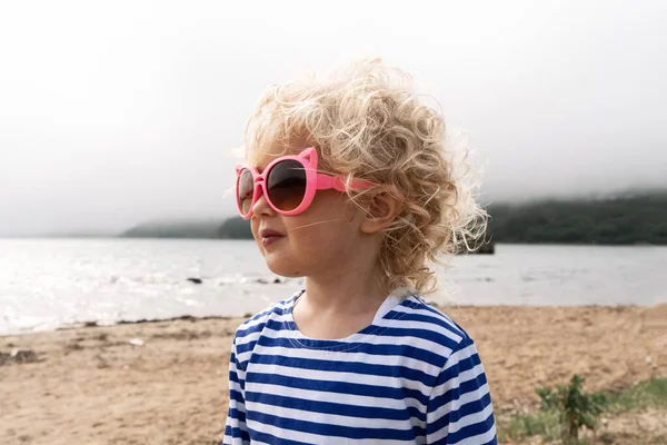 Una chica con el pelo rubio en gafas de sol está en el viento . — Foto de Stock