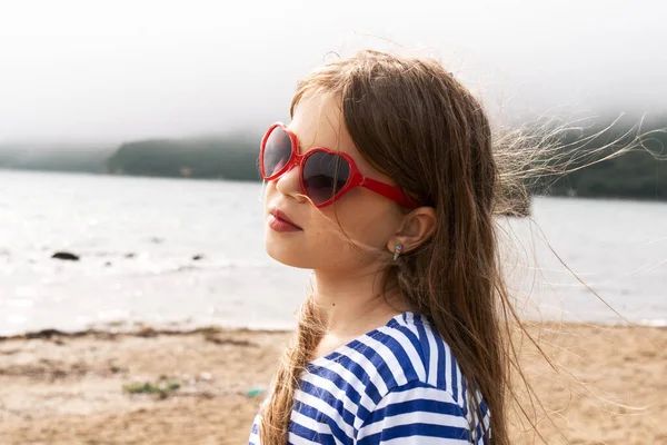 Una chica con el pelo rubio en gafas de sol está en el viento . — Foto de Stock