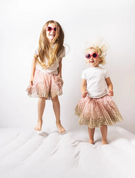 Niñas con gafas de sol y vestidos idénticos están saltando sobre un colchón blanco . — Foto de Stock