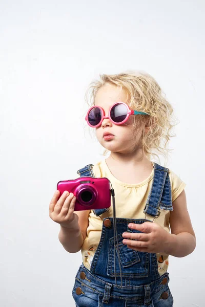 Niña en gafas de sol de color rosa y una cámara de bebé rosa . — Foto de Stock